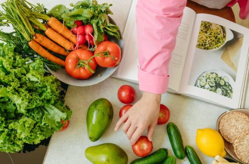 Top view of fresh vegetables and hands arranging them with a recipe book, promoting healthy eating.
