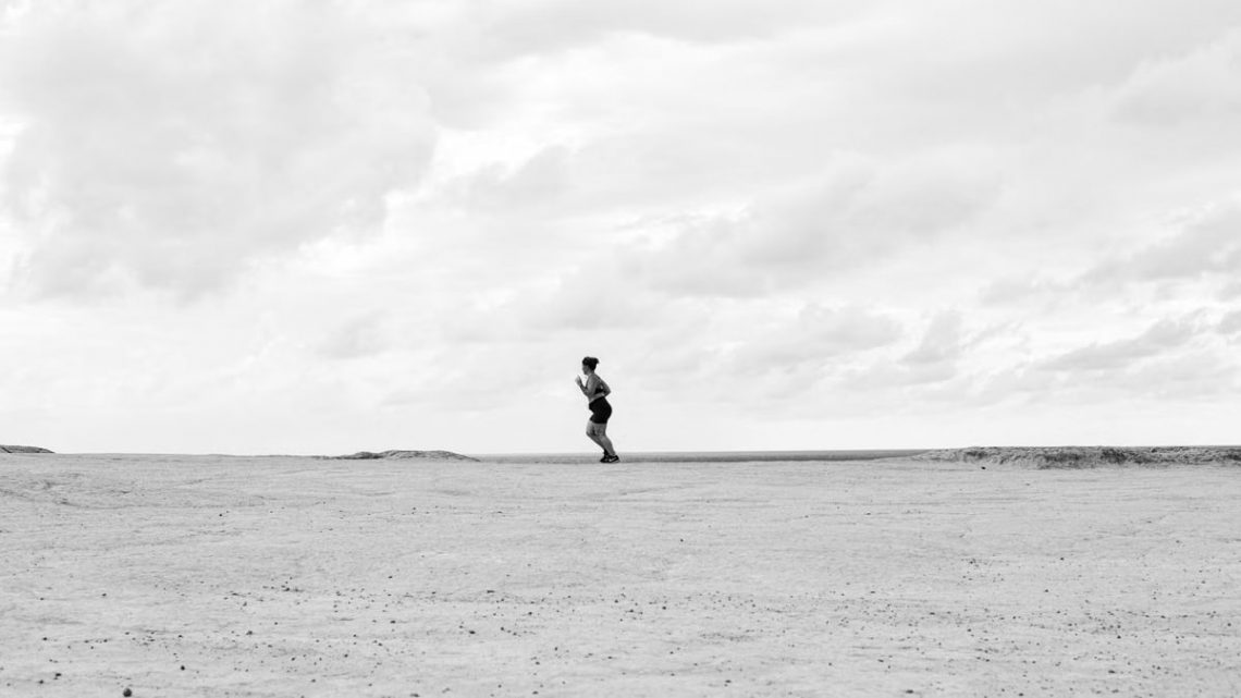 Black and white photo of a lone person running on a vast barren landscape in Natal, Brazil.
