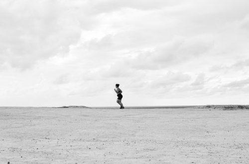 Black and white photo of a lone person running on a vast barren landscape in Natal, Brazil.